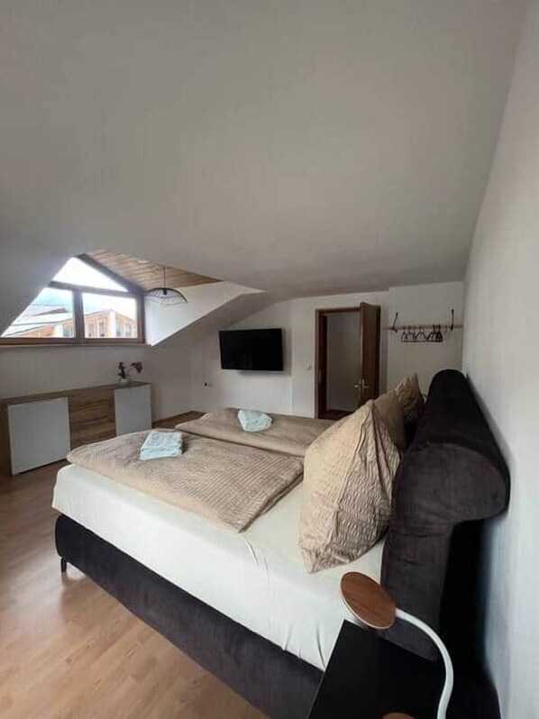A bedroom with a loft-style ceiling, a bed with beige bedding, a dark headboard, and a wooden floor. - Apartment mit Bergblick (Aldrans)