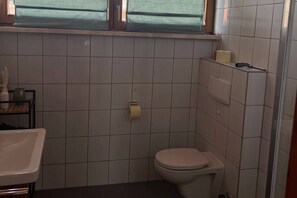 A small bathroom with a toilet, a shelf with toiletries, and a window above the toilet. - Apartment mit Bergblick (Aldrans)