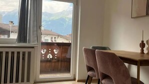 A room with a wooden dining table and two chairs, a window with a view of mountains, and a radiator. - Apartment mit Bergblick (Aldrans)
