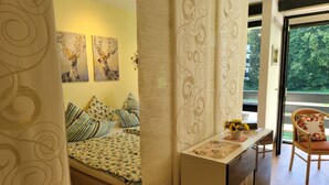 Een slaapkamer met een bed, kussens, een nachtkastje met een vaas zonnebloemen en uitzicht op groen.