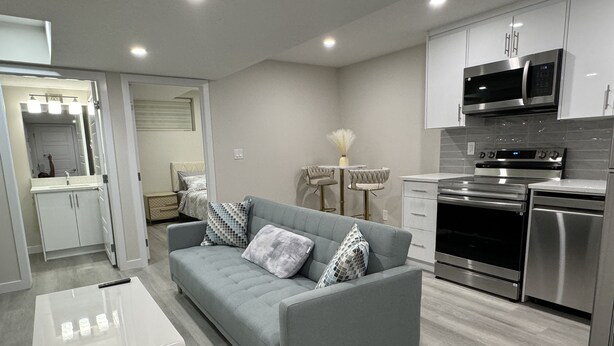 A modern kitchen with stainless steel appliances, a grey sofa with patterned cushions, and a small dining area with a white vase. - Brand new 2 bdrm 3 beds luxury Guest Suite with separate entrance (Calgary)