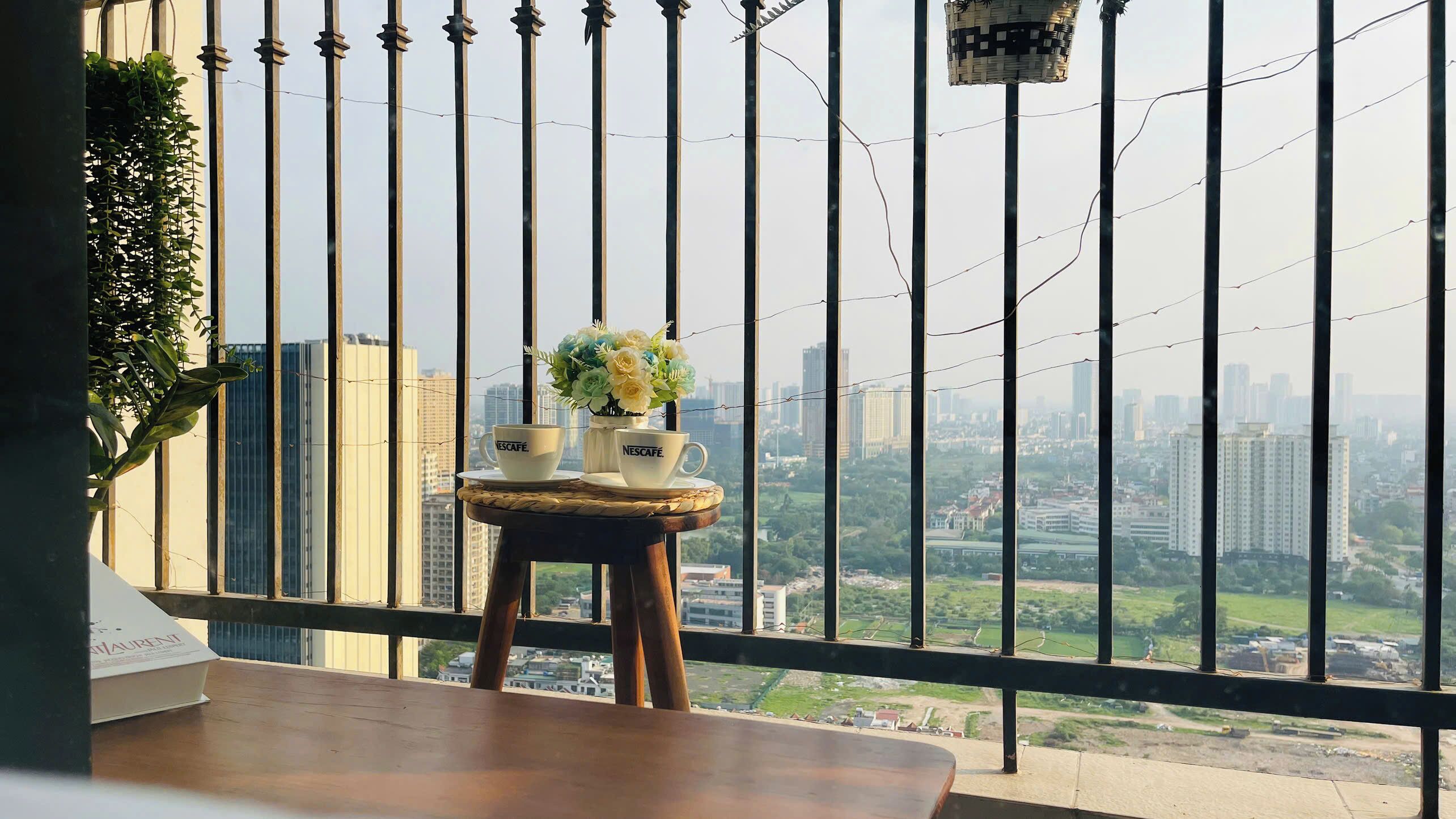 A balcony with a table, two Nescafe cups, and a vase of flowers.