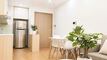 Een moderne keuken met een inbouwkoelkast, een eethoek met tafel en stoelen, en een zithoek met een bank en een potplant.