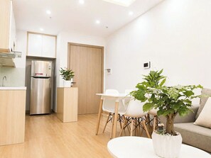 Una cocina moderna con refrigerador integrado, un comedor con mesa y sillas, y una sala de estar con sofá y planta en maceta.