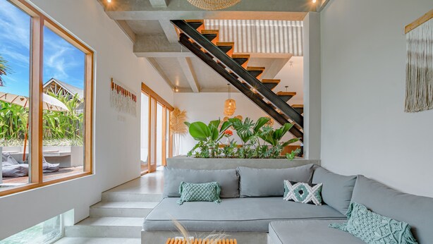 A modern living room with a grey sofa, a wooden coffee table, and a staircase leading to an upper level. - Octo 5 Villa by Betterplace (Canggu)