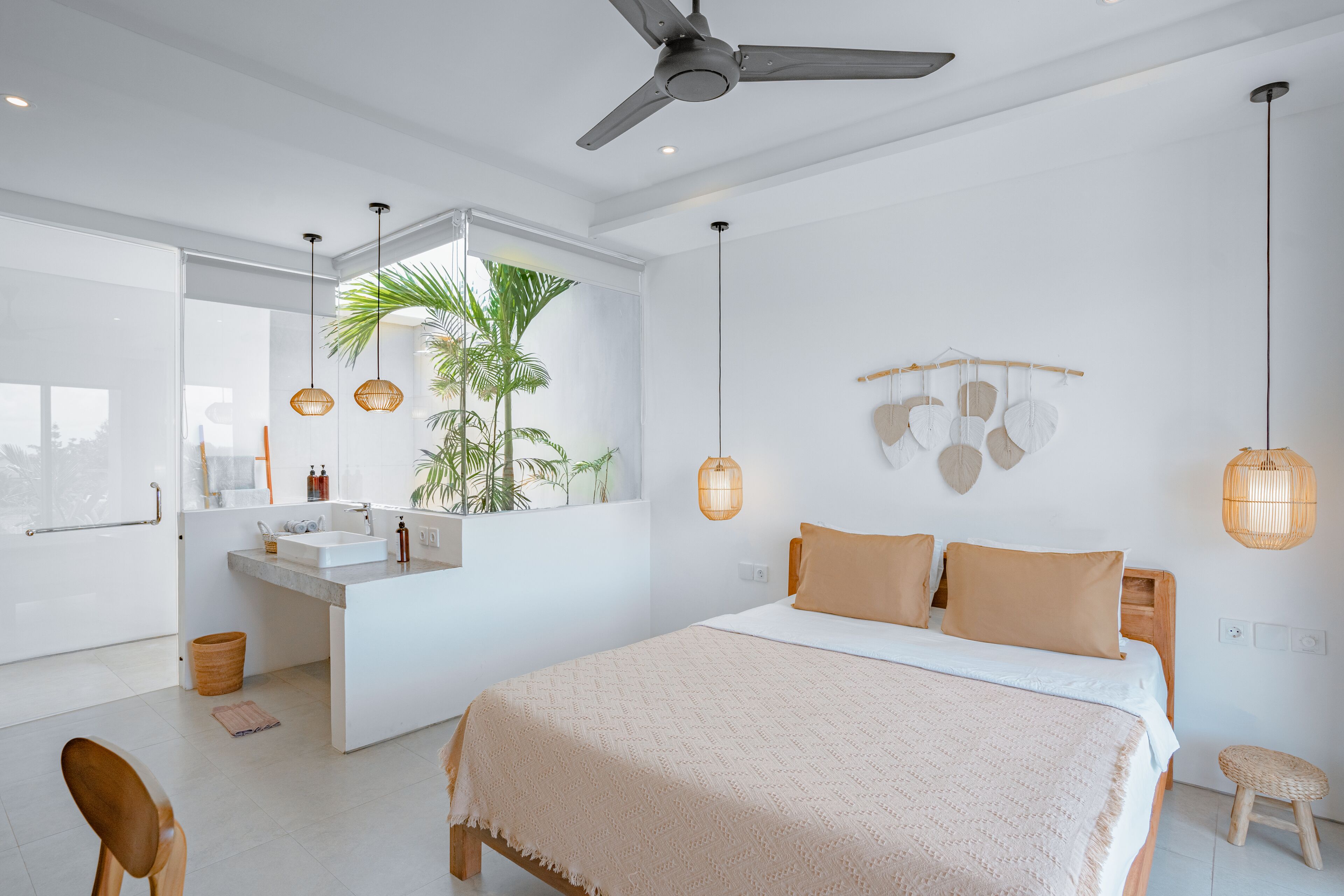 Een moderne slaapkamer met een groot bed, een badkamer met een wastafel en een plafondventilator.