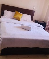 A neatly made bed with white bedding and a single yellow pillow.