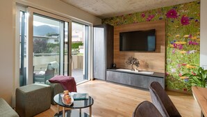 Un soggiorno moderno con una grande TV montata su una parete in legno, una porta scorrevole in vetro che dà su un balcone e una carta da parati fiorata e colorata.