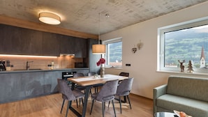 Una cucina moderna con mobili scuri, un tavolo da pranzo in legno e vista su una chiesa tramite un'ampia finestra.