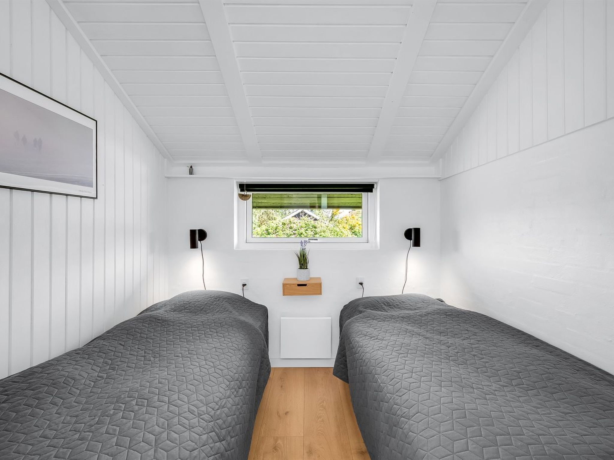Een kamer met twee bedden, een raam met uitzicht op groen en een wandplank met een plant.