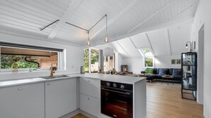 Une cuisine moderne dotée d’un four encastré, un coin repas avec une table et des chaises, et une vue sur l’extérieur.