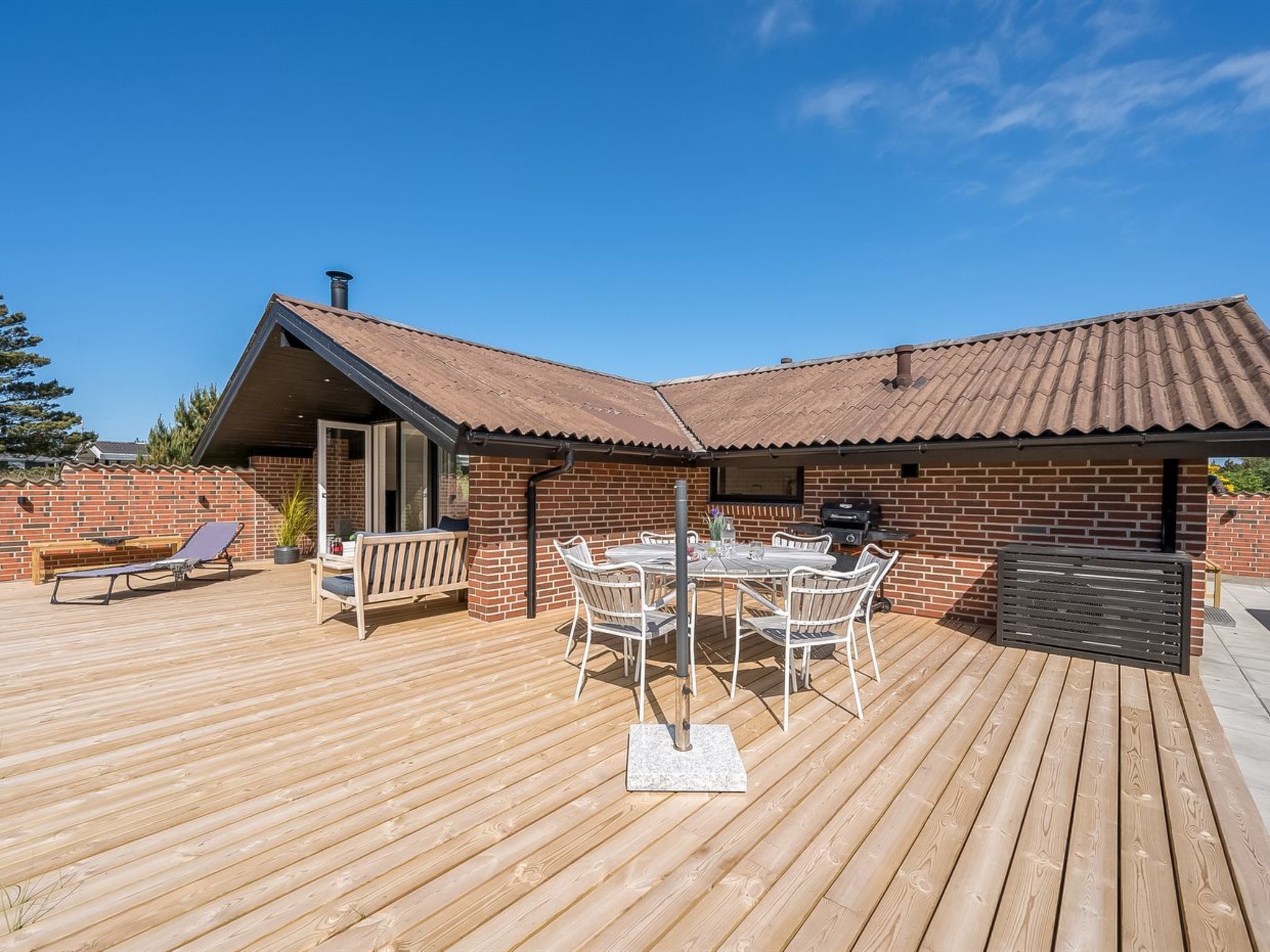 Eine Holzterrasse mit einem Backsteinhaus, einem Grill und Gartenmöbeln.
