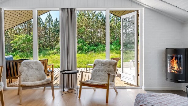 Une pièce chaleureuse avec une grande porte-fenêtre coulissante donnant sur une terrasse, deux fauteuils confortables, une petite table ronde et une cheminée.