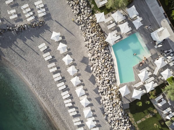 Vue aérienne d’un complexe hôtelier avec une piscine, des parasols de plage et des chaises longues.