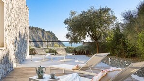 A wooden deck with lounge chairs, a table with a teapot, and a view of a mountainous landscape.