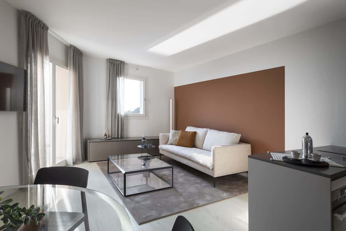 Una sala de estar moderna con una mesa de centro de vidrio, un sofá, una mesita auxiliar y una zona de cocina con un hervidor.