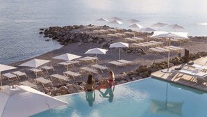 Una piscina infinita con sillones y sombrillas, una costa rocosa y vistas al mar.