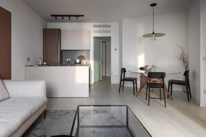 A modern kitchen with a central island, a dining area with a round table and chairs, and a living area with a sofa and a glass coffee table.