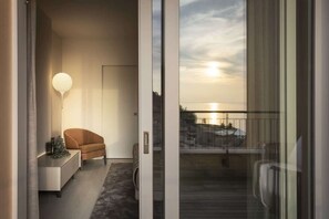 Et moderne interiør med en sofa, en lampe og udsigt til solnedgangen fra en balkon.