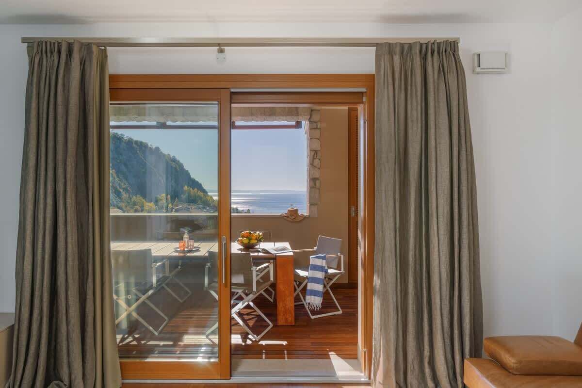Una habitación con puerta corrediza de vidrio que da a un espacio exterior con mesa, sillas y vista de un paisaje montañoso.