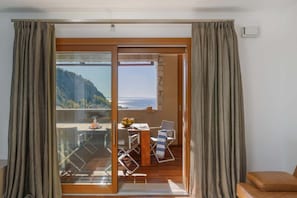 Una stanza con una porta scorrevole in vetro che si apre su uno spazio esterno con tavolo, sedie e vista su un paesaggio montuoso.