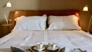 A neatly made bed with white linens, two bedside lamps, and a tray with two cups and saucers.