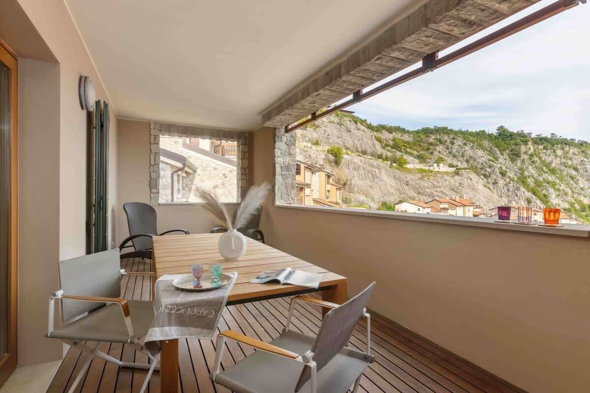 Un balcon avec une table à manger, des chaises et une vue sur une colline.