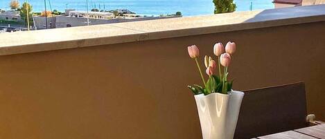 Una mesa con un florero y una revista abierta, con vista al mar, un muro de piedra y un cielo despejado.