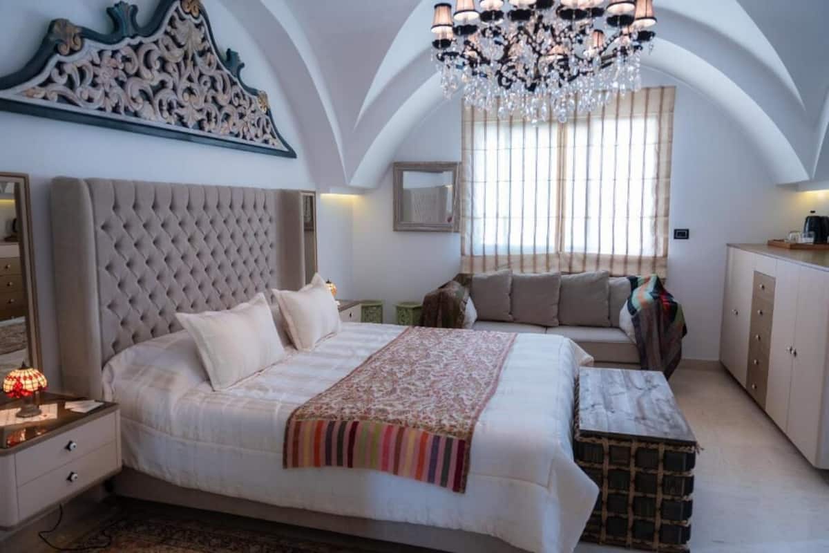 Um quarto espaçoso com uma cama grande, um candelabro e vista para o exterior através de uma janela com persianas.