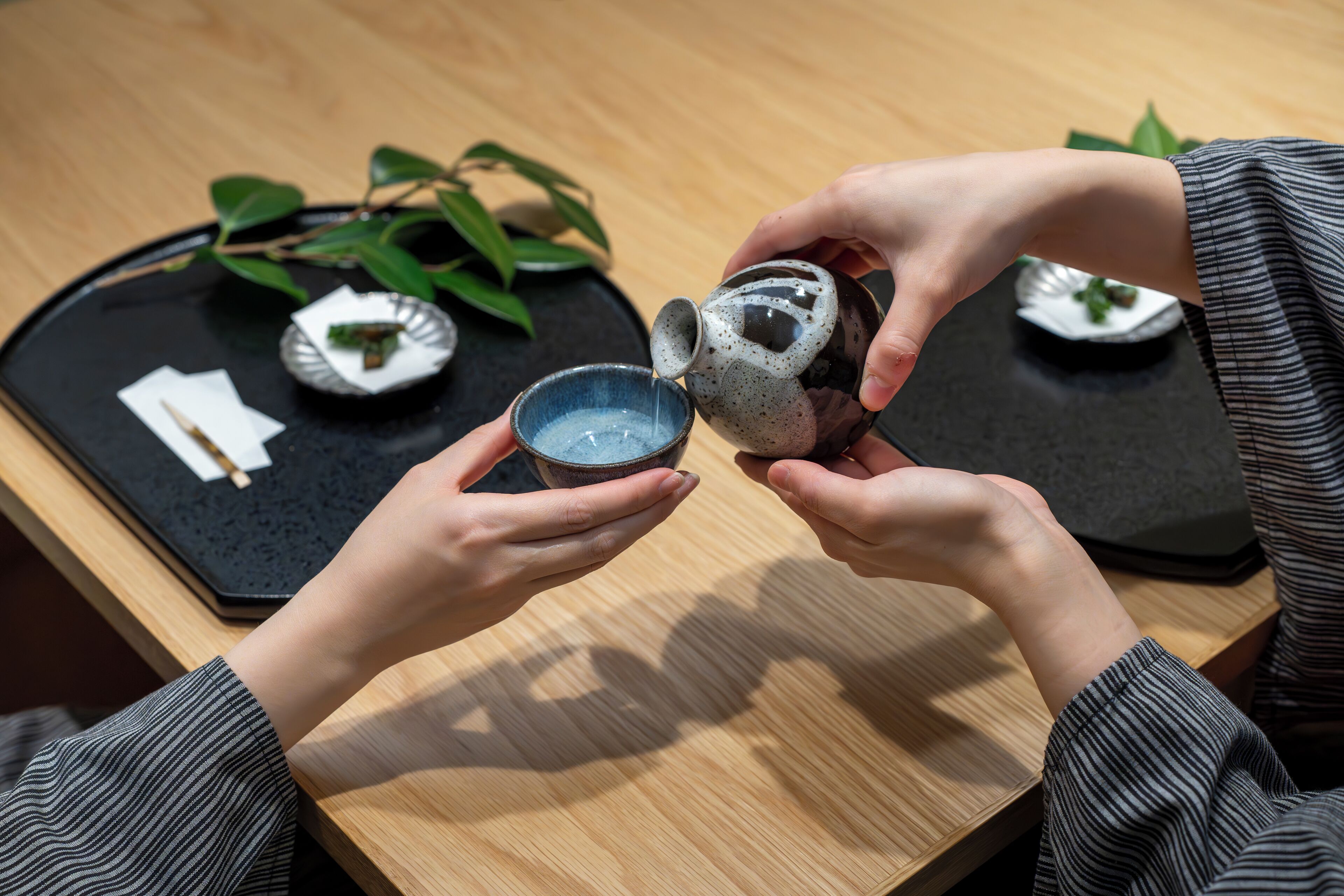 A person pouring liquid from a ceramic pitcher into a small bowl.