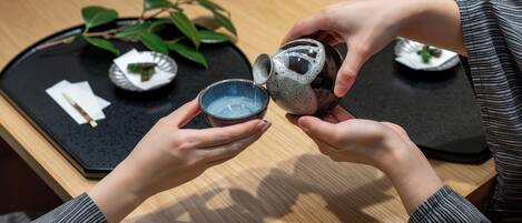 A person pouring liquid from a ceramic pitcher into a small bowl.