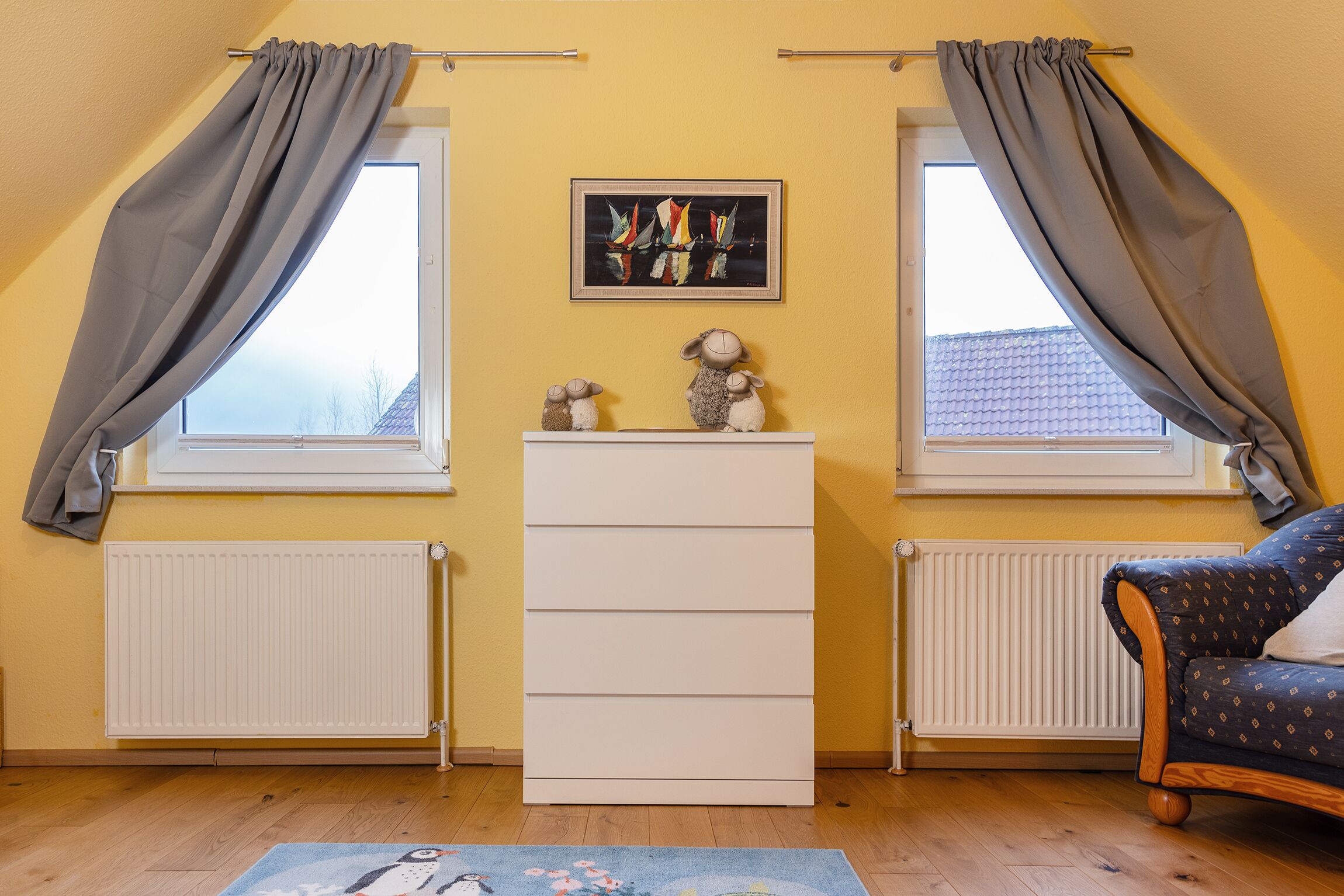 Et værelse med to vinduer, en radiator, et skrivebord og en sofa.