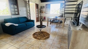 A spacious living area with a blue sofa, a dining table with chairs, and a kitchen area with a TV.