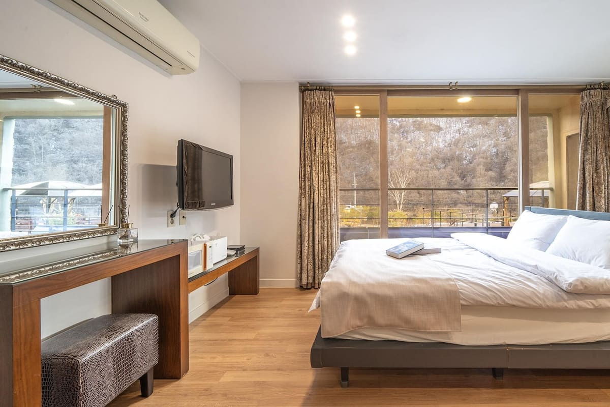 Ein Schlafzimmer mit einem Bett, einem Fernseher, einem Schreibtisch und einem Fenster mit Vorhängen.
