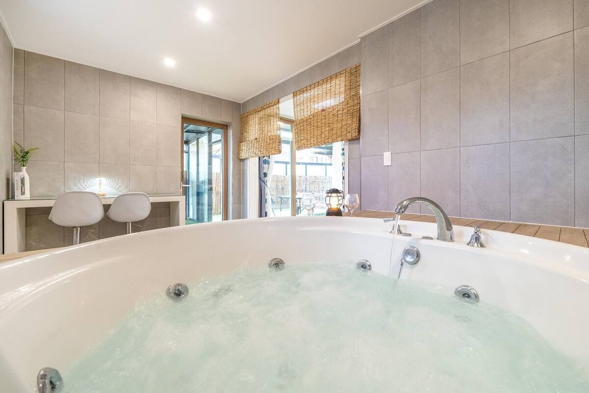 Ein modernes Badezimmer mit einer großzügigen Badewanne, einem Waschtisch mit Spiegel und einer Sitzecke mit zwei Stühlen.