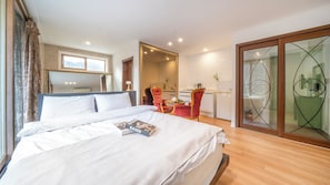 Une chambre d’hôtel avec un lit, un petit coin salon avec un fauteuil, un miroir et une vue sur l’extérieur.