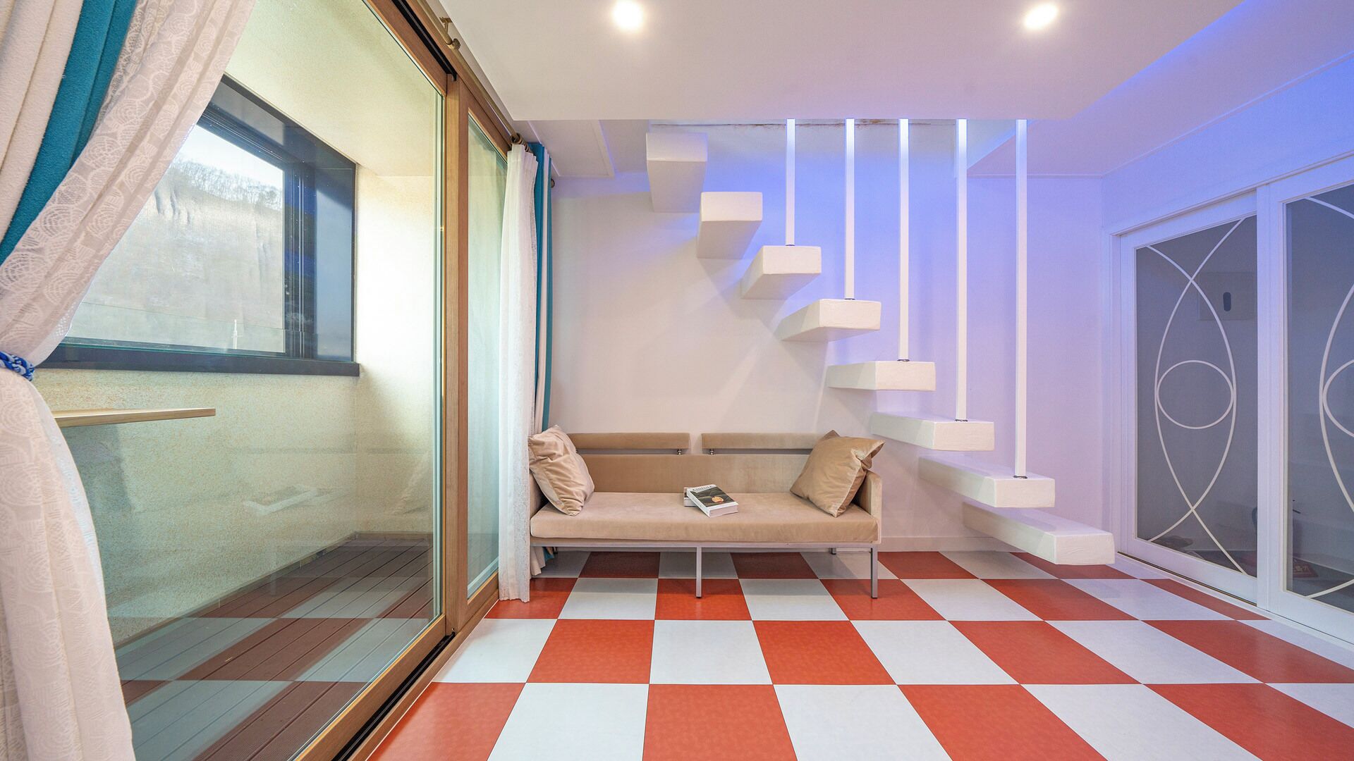 Un interior moderno con piso a cuadros, un sofá con cojines y una escalera con lámparas colgantes.