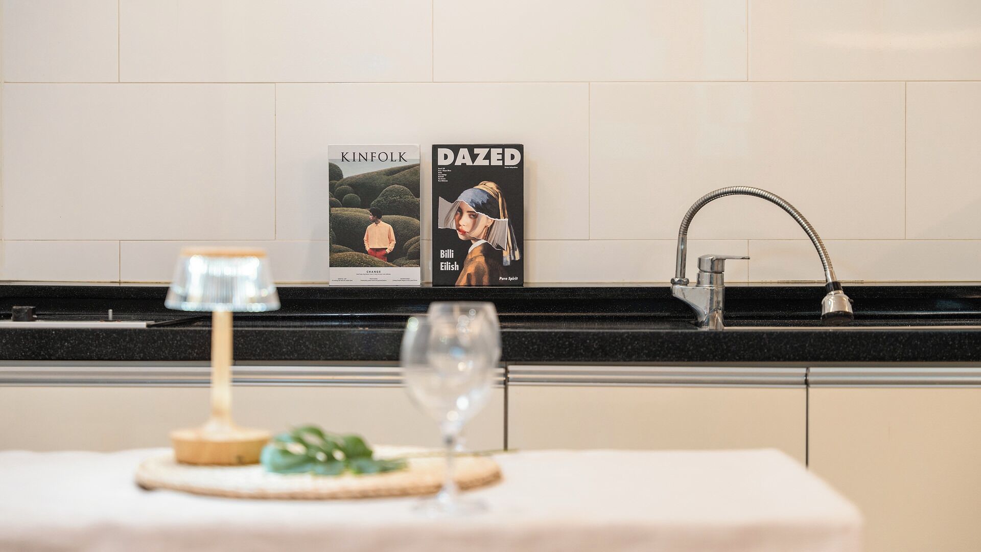 A kitchen counter with a wine glass, a candle, and two magazines.