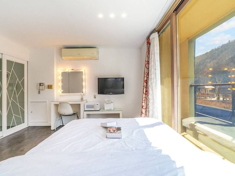 Habitación de hotel con una cama, un escritorio con computadora, televisión y un ventanal con vista a la ciudad.