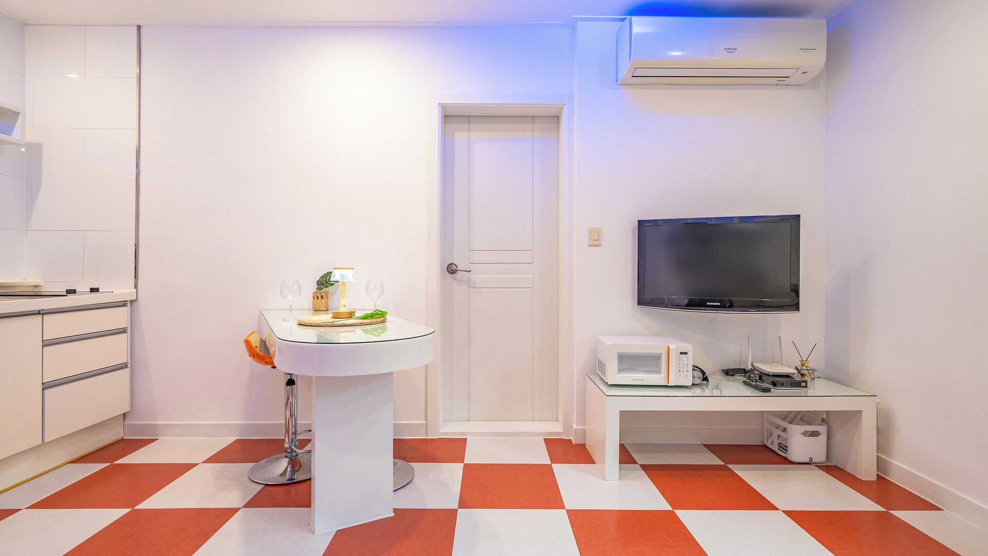 A modern kitchen with a microwave, a small table with a lamp, and a TV mounted on the wall.