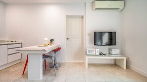 Une pièce compacte comprenant un coin cuisine, un espace repas avec une table et des chaises, un téléviseur et une porte blanche.