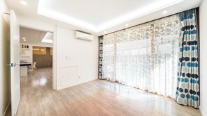 Une pièce spacieuse dotée d’un plancher en bois, d’une porte-fenêtre coulissante avec des rideaux à motifs et d’un coin cuisine visible, équipé d’un four à micro-ondes.