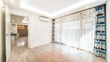 Amplia habitación con piso de madera, puerta corredera de vidrio con cortinas estampadas y una cocina visible que incluye un microondas.