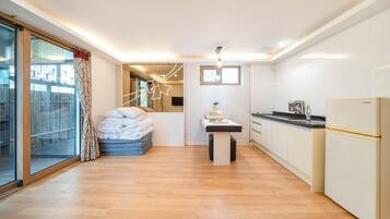A compact kitchen with a refrigerator, a dining table, and a window with curtains.