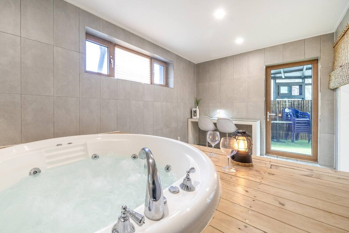 Ein modernes Badezimmer mit einer freistehenden Badewanne, Holzboden und Blick ins Freie durch eine Glastür.