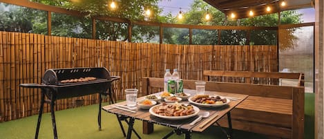 An outdoor patio with a barbecue grill, wooden table, and chairs.