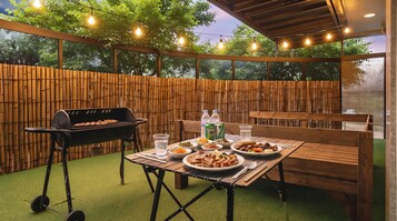 An outdoor patio with a barbecue grill, wooden table, and chairs.