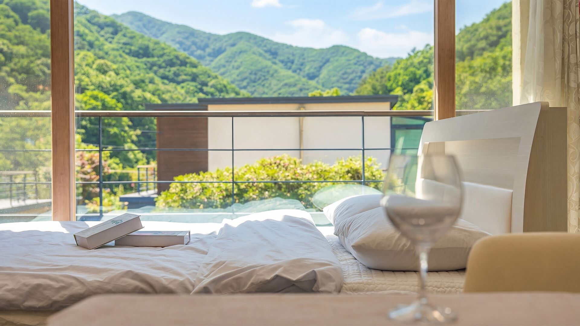 A bedroom with a bed, a glass of wine, and a book on the bed. The room has a view of green hills and a balcony.