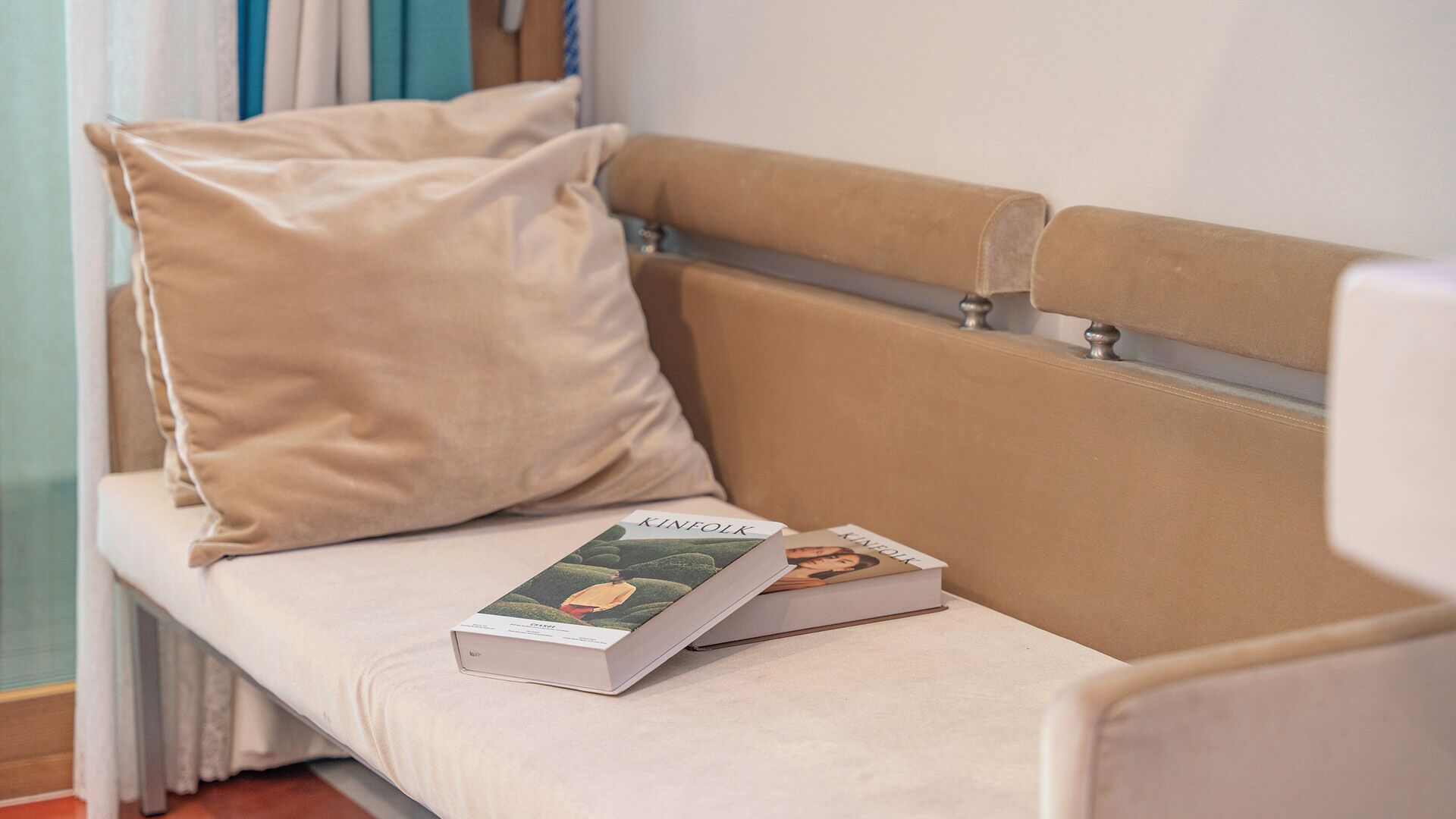 A beige sofa with a cushion, two books titled 'KINFOLK' and 'KANSAS,' and a window with curtains.