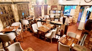 A restaurant with wooden tables and chairs, stone walls, and a brick oven. - Auberge Thais (Toudja)